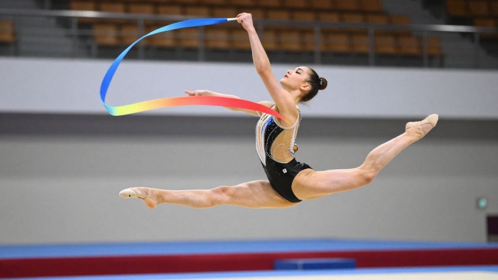 Gimnastă ritmică executând un salt cu panglica.