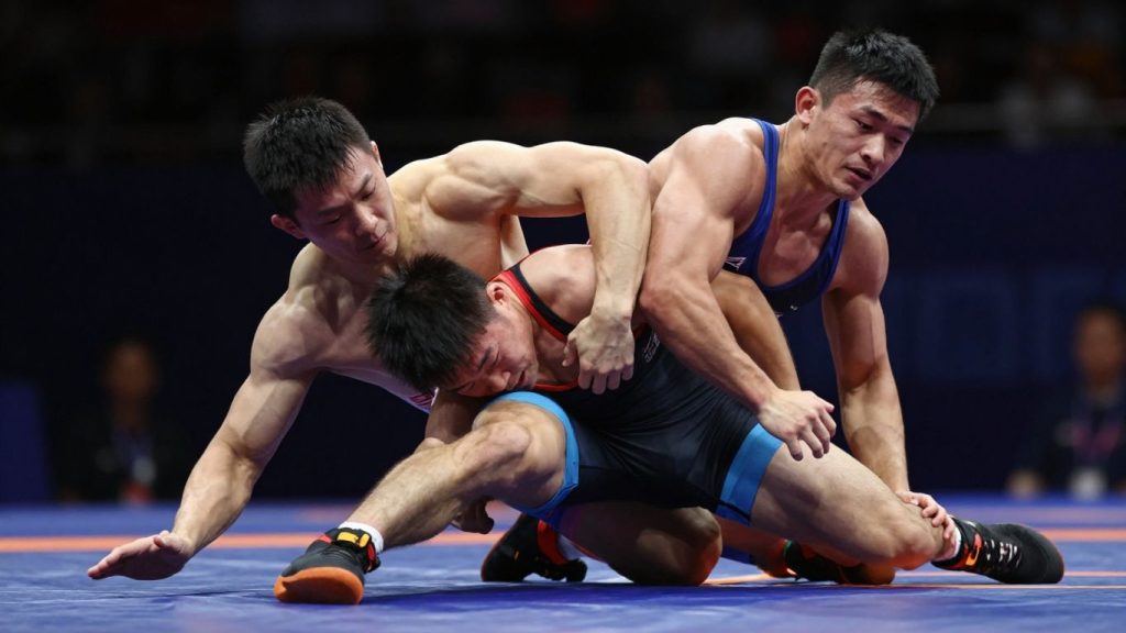 Doi luptători olimpici în acțiune pe saltea.