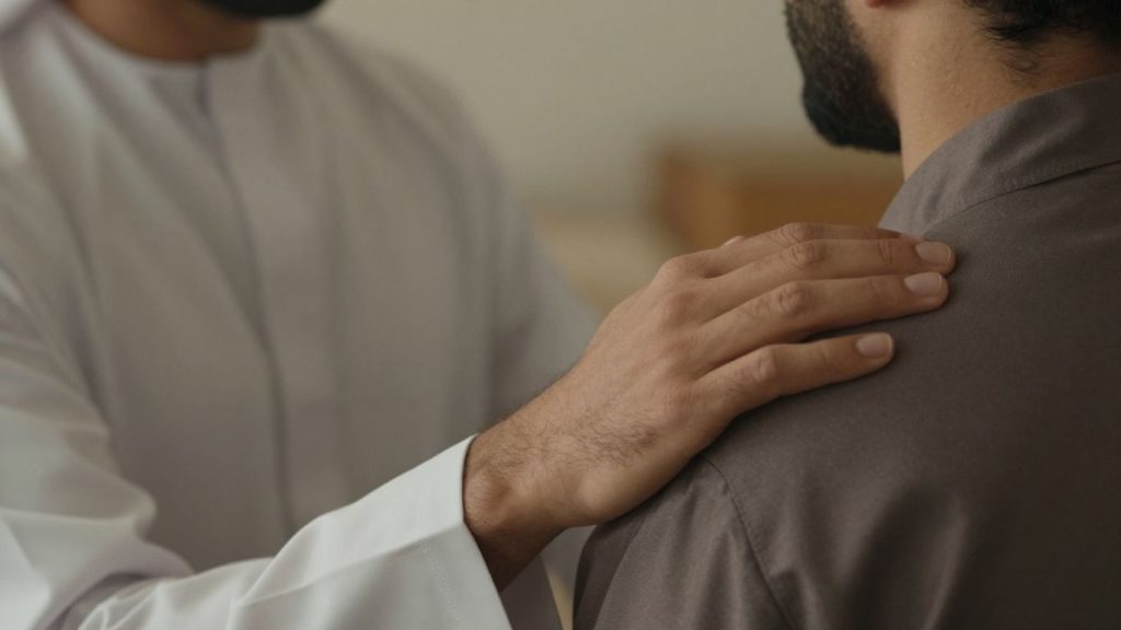 O persoană pune o mână pe umărul alteia.